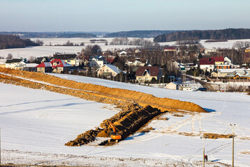 Road construction. Orange Excavator digs a trench for laying a sewer pipe on a cloudy winter day. Selective focus, shallow depth of field in the village