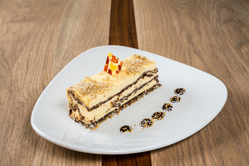 Elegant layered dessert on a white plate topped with nuts and a decorative piece of chocolate
