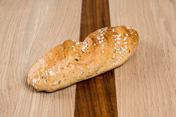 Rustic bread roll with seeds resting on a two tone wooden surface perfect for a simple snack