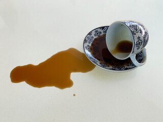 Spilled coffee from patterned ceramic cup on white surface