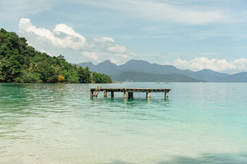 A dock is floating in the water next to a beach. The water is calm and the sky is clear