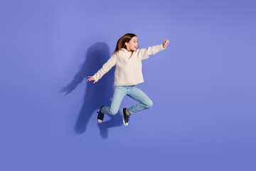 Obraz premium Preteen girl in stylish sweater jumping joyfully against a vibrant violet background, showcasing youthful energy and happiness