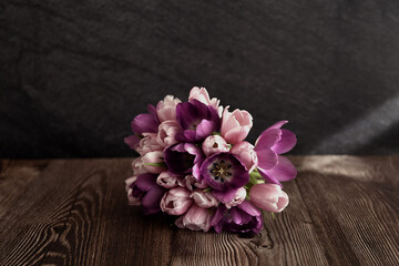 a bouquet of tulips located on a wooden table against a dark wall. Tulips of different shades - from dark purple to soft pink and white