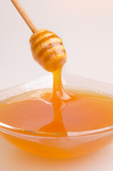 A transparent plate is filled with honey. A wooden spoon lifts the honey