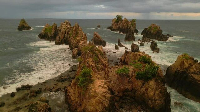 Drone aerial view of Sharks Teeth Beach with its jagged rock formations and crashing waves at sunset