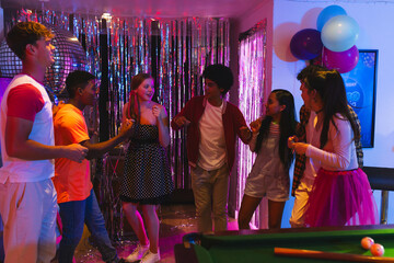 Diverse teen friends dancing and laughing at vibrant party with decorations and balloons, at home