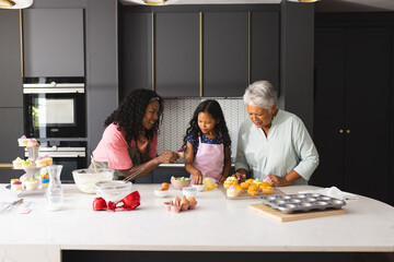 Three diverse generations baking cupcakes in modern kitchen, sharing joyful moments, at home