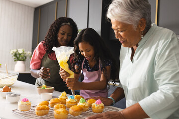 Three diverse generations decorating cupcakes , enjoying baking in modern kitchen, at home