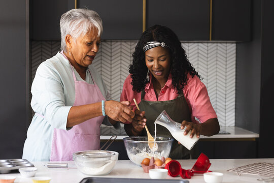 Baking in kitchen, diverse grandmother and child mixing ingredients with joy, at home