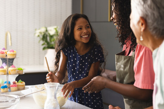 Three diverse generations baking in kitchen, sharing smiles and making cupcakes, at home