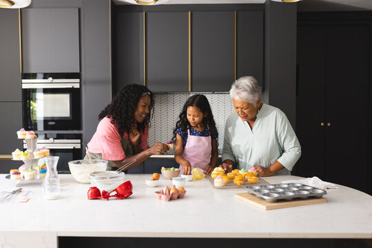 Three diverse generations baking cupcakes in modern kitchen, sharing joyful moments, at home