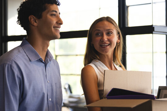 Diverse colleagues smiling and talking while carrying boxes in modern office setting
