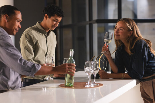Diverse colleagues enjoying wine and conversation at modern office bar after work