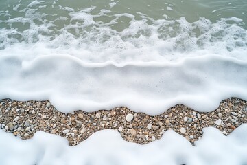 Obraz premium Waves gently lap against a rocky shoreline with white foam during a tranquil daytime at the beach