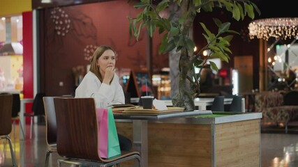 Lady sitting alone at a table in a mall dining area, with a drink, fries, and an open book, captured in a cozy, relaxed moment with a vibrant background featuring mall atmosphere