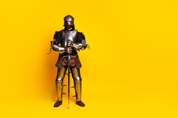 Medieval knight in full armor posing on bright yellow background with noble stance
