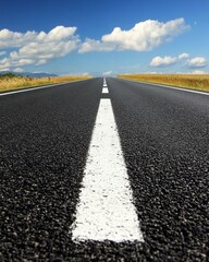 Fototapeta premium Endless Asphalt Road Journey Under a Bright Blue Sky with Fluffy Clouds and Golden Wheat Fields on the Horizon