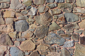 Natural stone wall displays an array of textures and colors under sunlight in a serene setting