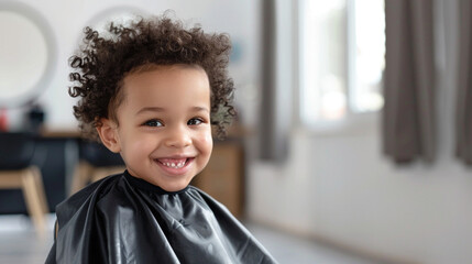 Kid African-American child sitting in a barber’s chair, smiling during haircut with salon on background. Childhood, grooming joy concept. Fun, carefree family-friendly atmosphere