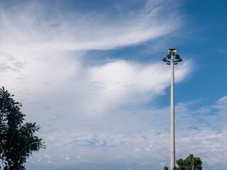 High street light pole made of metal with street light installed on it, near by are lush green trees. Amazing cloudy blue sky as background. Street lights are very functional as public safety.