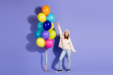 Playful young girl posing with colorful balloons against a purple backdrop