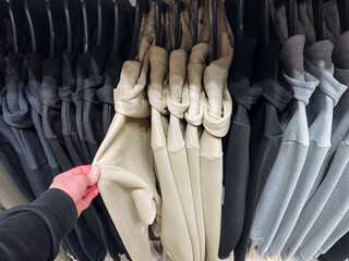 A person is holding a shirt right in front of a carefully arranged row of various shirts,...