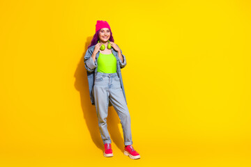 Young cheerful woman in colorful outfit with pink beanie and bright yellow background showcasing trendy fashion and casual style