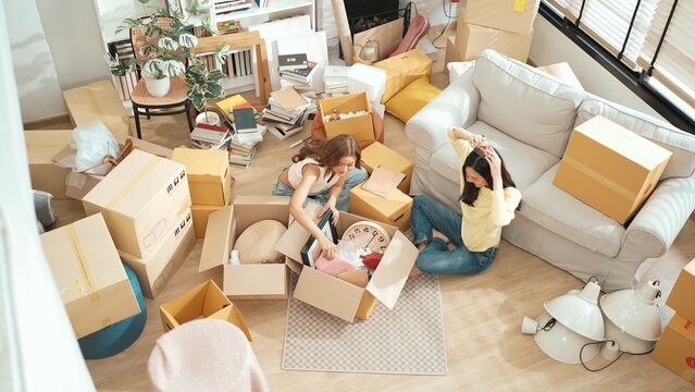 Top view of happy friend unpacking box and picking furniture together. Attractive teenager moving to new apartment while plating talking at living room surrounded with cardboard box. Estate. Myrmidon.