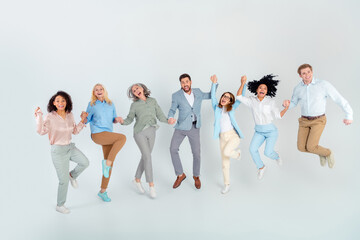 Naklejka premium Diverse group of professionals jumping together in enthusiasm against light background, multi-age