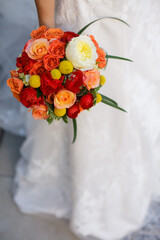 Bride holding a vibrant bouquet of red, orange, and yellow flowers