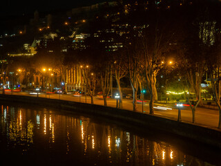 Tbilisi at night. Night cityscape. View of the Kura River from the bridge. Road and lanterns. Ancient city.