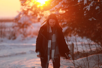 young woman walking in a snowy winter forest at sunset. dressed in a black leather jacket and a checkered shirt. frosty weather in a pine forest. lots of snow and sun. Christmas holiday