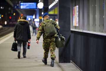 Swiss Army soldier with luggage walking on platform of railway station at Swiss City of Zürich on a dark winter night. Photo taken February 16th, 2025, Zurich Oerlikon, Switzerland.