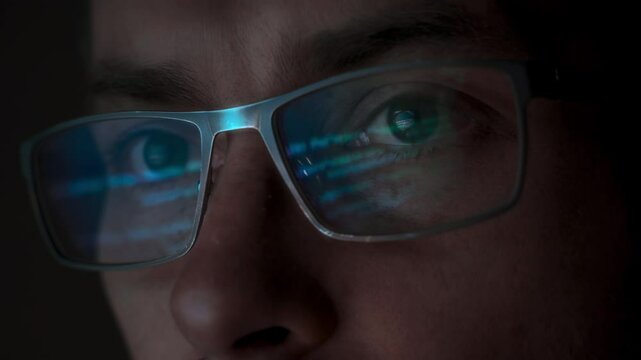 Close-up of a data scientist, wearing eyeglasses, reflecting programming code on the lenses. Computer science machine learning and AI concept. 