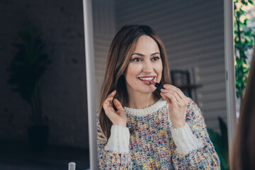 Smiling young woman applying lipstick in front of a mirror at home during a peaceful day.