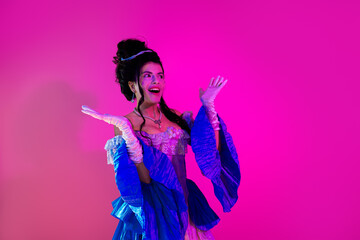 Fototapeta premium Young woman dressed in an elegant royal costume with glowing neon hues on a vibrant pink backdrop