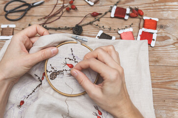 Woman is embroidering larch branches and hawthorn berries with a needle. Handmade embroidery process.