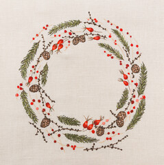 Hand-embroidered Christmas wreath. The wreath is made of larch and spruce branches, hawthorn berries, and cranberries.  Festive background with space for your text.
