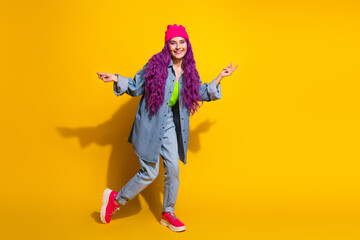 Playful young woman with vibrant style poses against a bright yellow background, showcasing pink hair and a cheerful personality