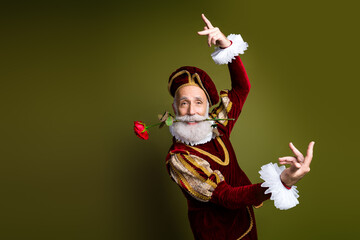 Elderly man in medieval attire posing gracefully with a rose on a khaki background