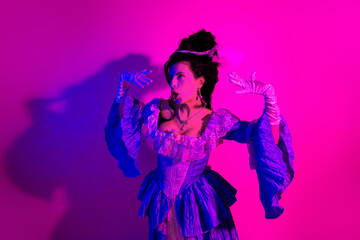 Elegant young woman in historical baroque costume posing under pink and ultraviolet light