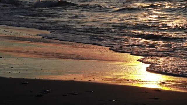 Close-up wave crashes onto the sand on a beach at golden sunset. Wavy Baltic sea. Normal speed with sound.