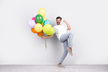 Fototapeta premium Young man celebrating enthusiastically holding colorful balloons against a white background, showcasing happiness