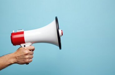 Hand holds white megaphone against blue background. Loudspeaker as tool for announcement, public speaking, marketing. Bullhorn for broadcasting, communication, advertising. Device for shouting.