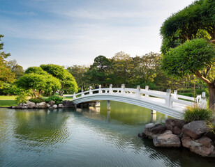 Fototapeta premium white bridge plants green trees stone decoration and water pond in public outdoor park
