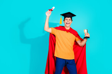 Cheerful male graduate holding trophy and certificate against vibrant blue background, wearing...