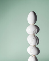 A tall stack of white eggs with transparent paint dripping down their surface against a pastel green background. A creative Easter concept.