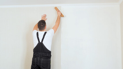 Skilled handyman carefully smoothing wallpaper with roller, ensuring precise application and professional finish during interior home improvement work
