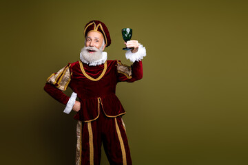 Senior man in Renaissance costume raising drink against khaki background