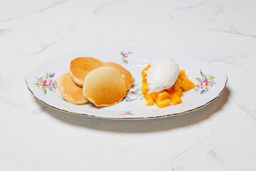Appetizing cheese pancakes with mango and ice cream on a large white plate